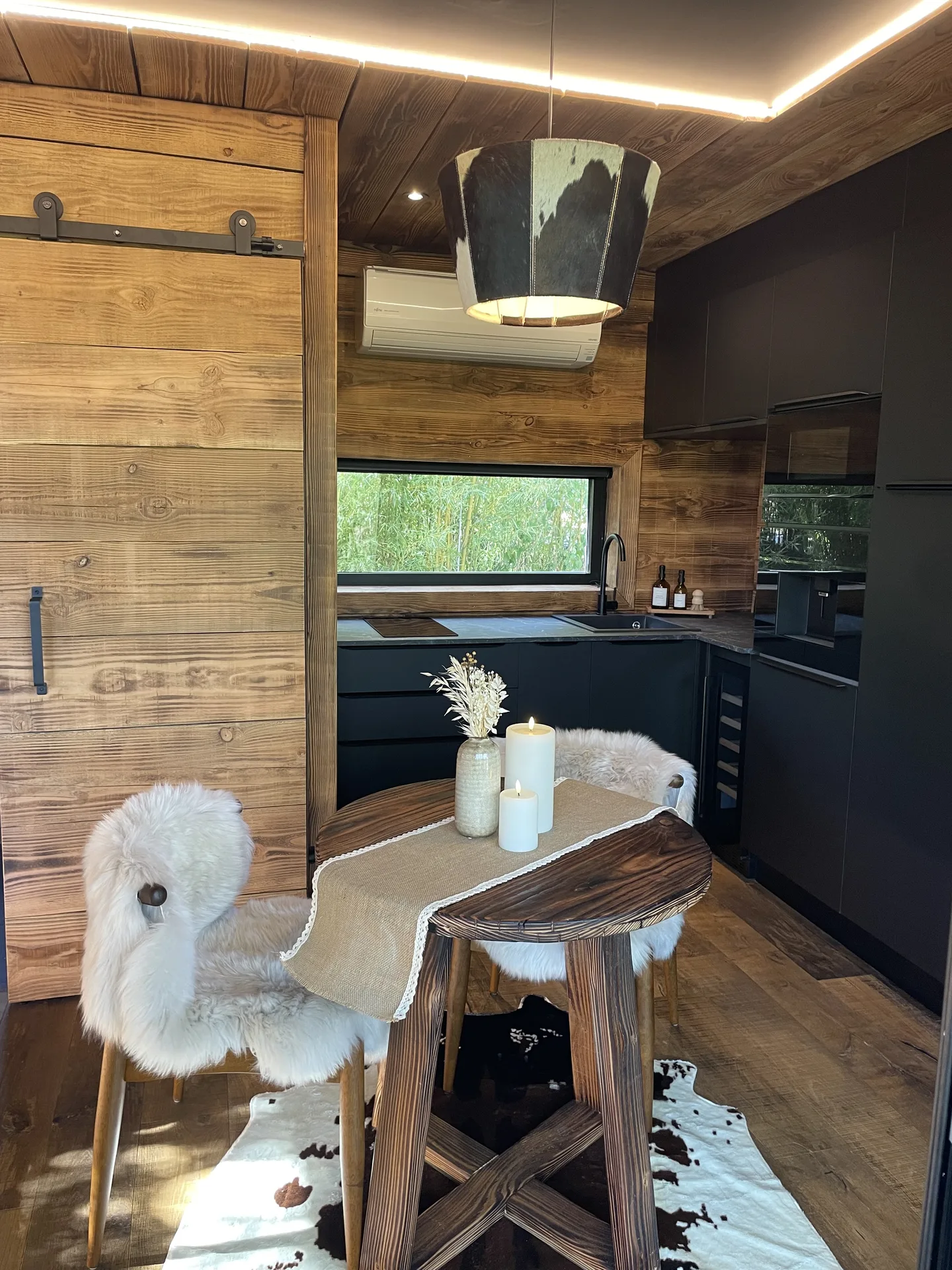 Coin repas avec table en bois brut, chaises habillées de peau de mouton et suspension design