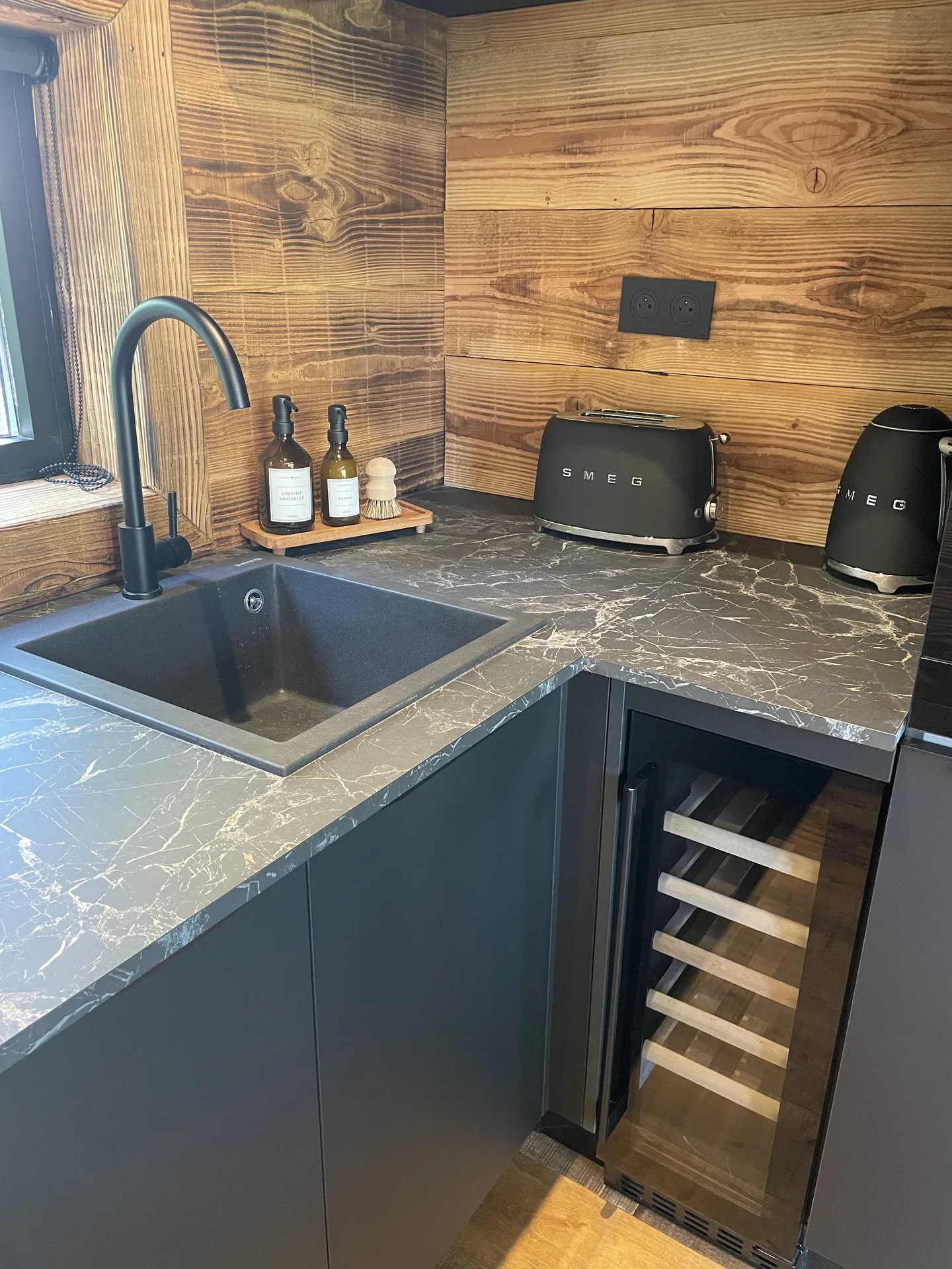 Cuisine équipée avec plan de travail en marbre, évier noir, cave à vin et petit électroménager design