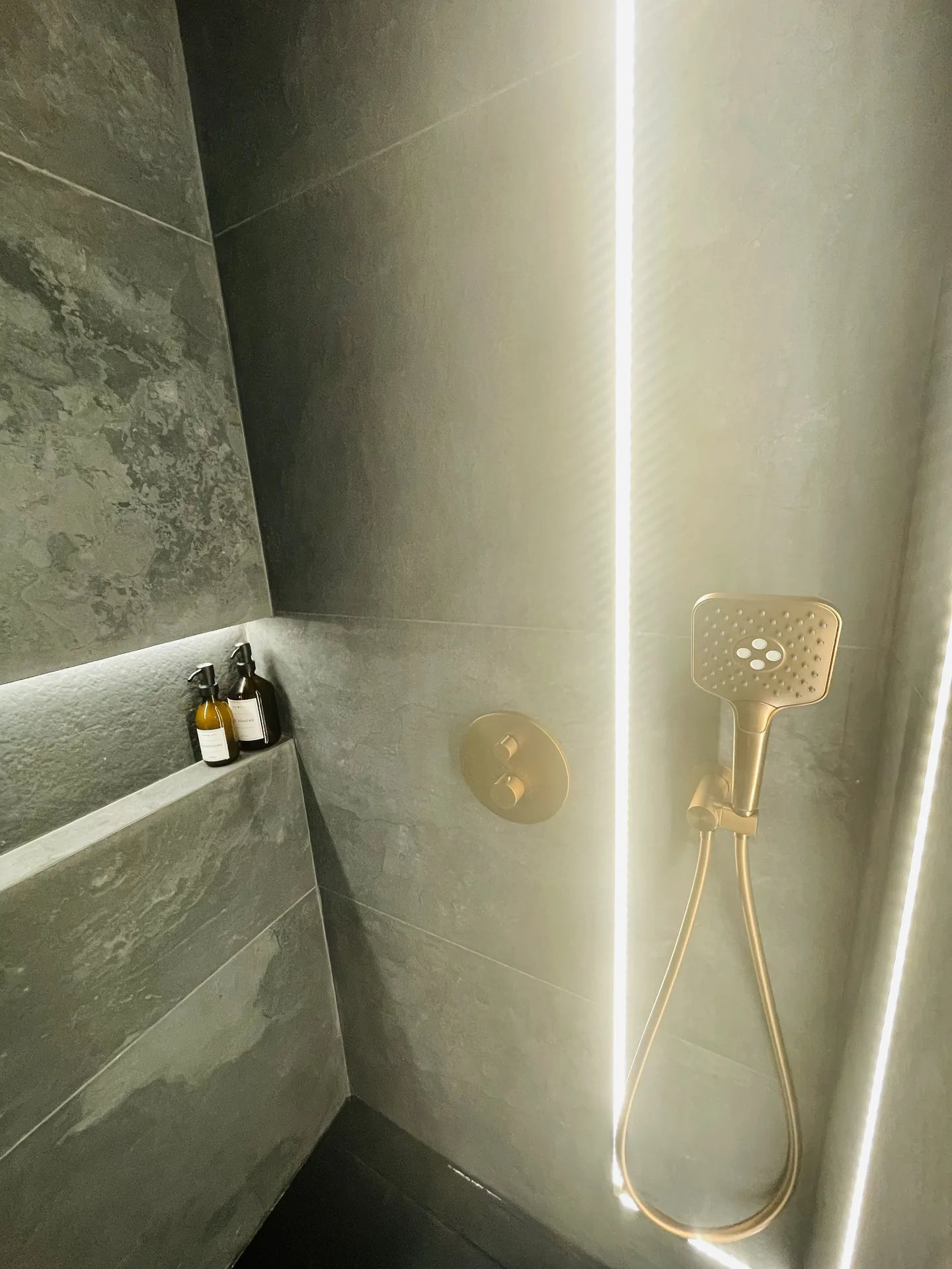 Douche à l'italienne carrelée pierre avec colonne lumineuse et douchette dorée