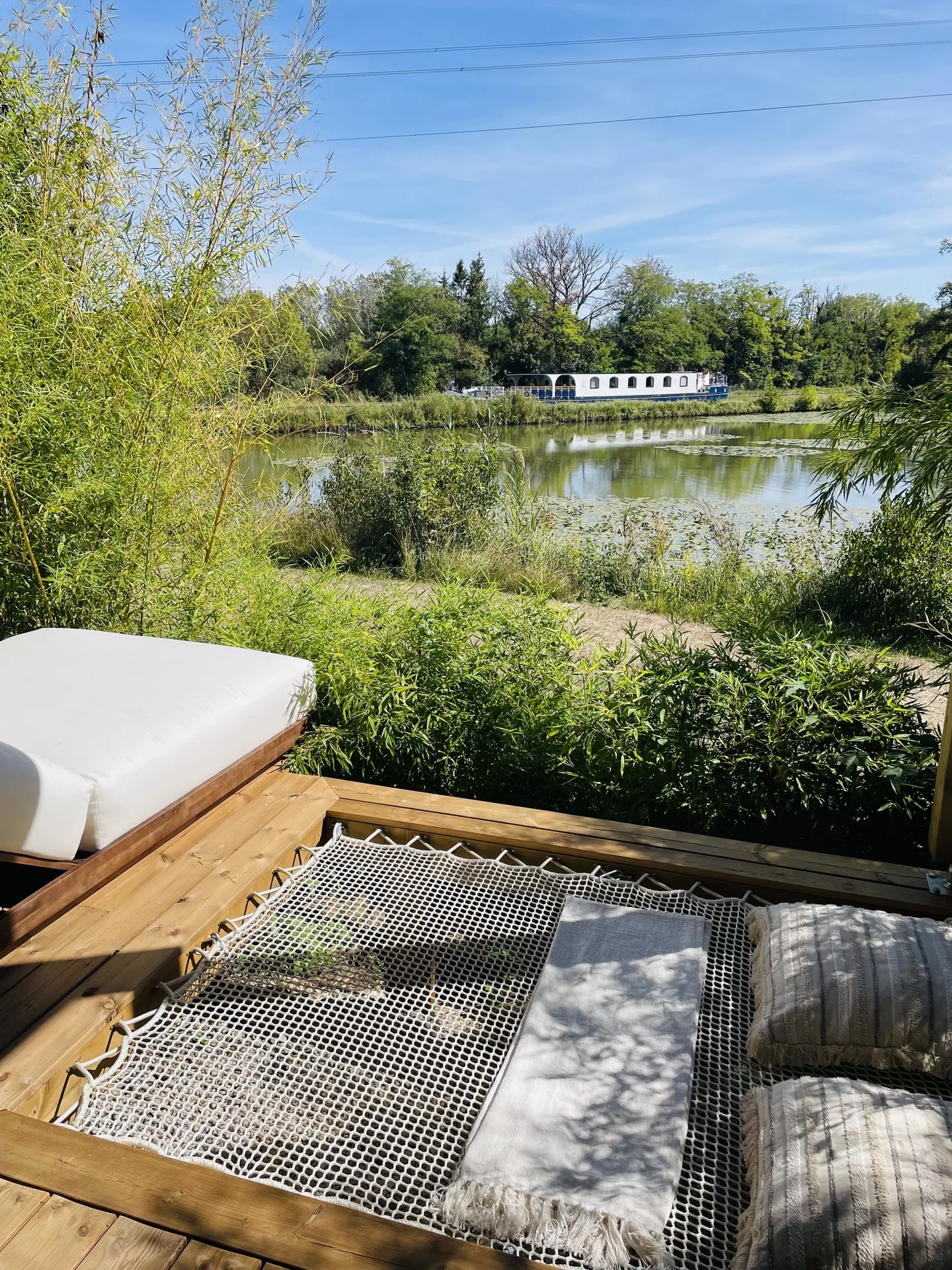 Vue depuis la terrasse sur le Canal de Briare, une péniche amarrée et un filet suspendu garni de coussins